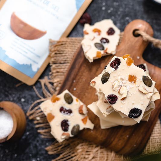 Köstliche weiße Schokoladenkekse mit getrockneten Früchten und Nüssen auf einem Holzbrett, dekoriert mit Fleur de Sel.