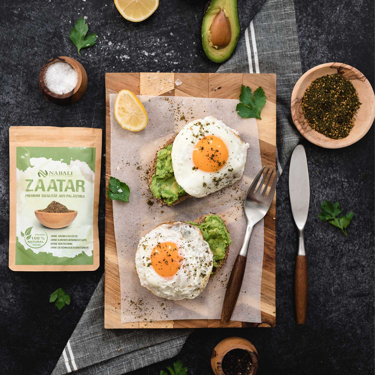"Avocado Toast mit Spiegelei, garniert mit Zaatar-Gewürz, serviert auf einem Holzbrett mit Zitrone und frischen Kräutern."