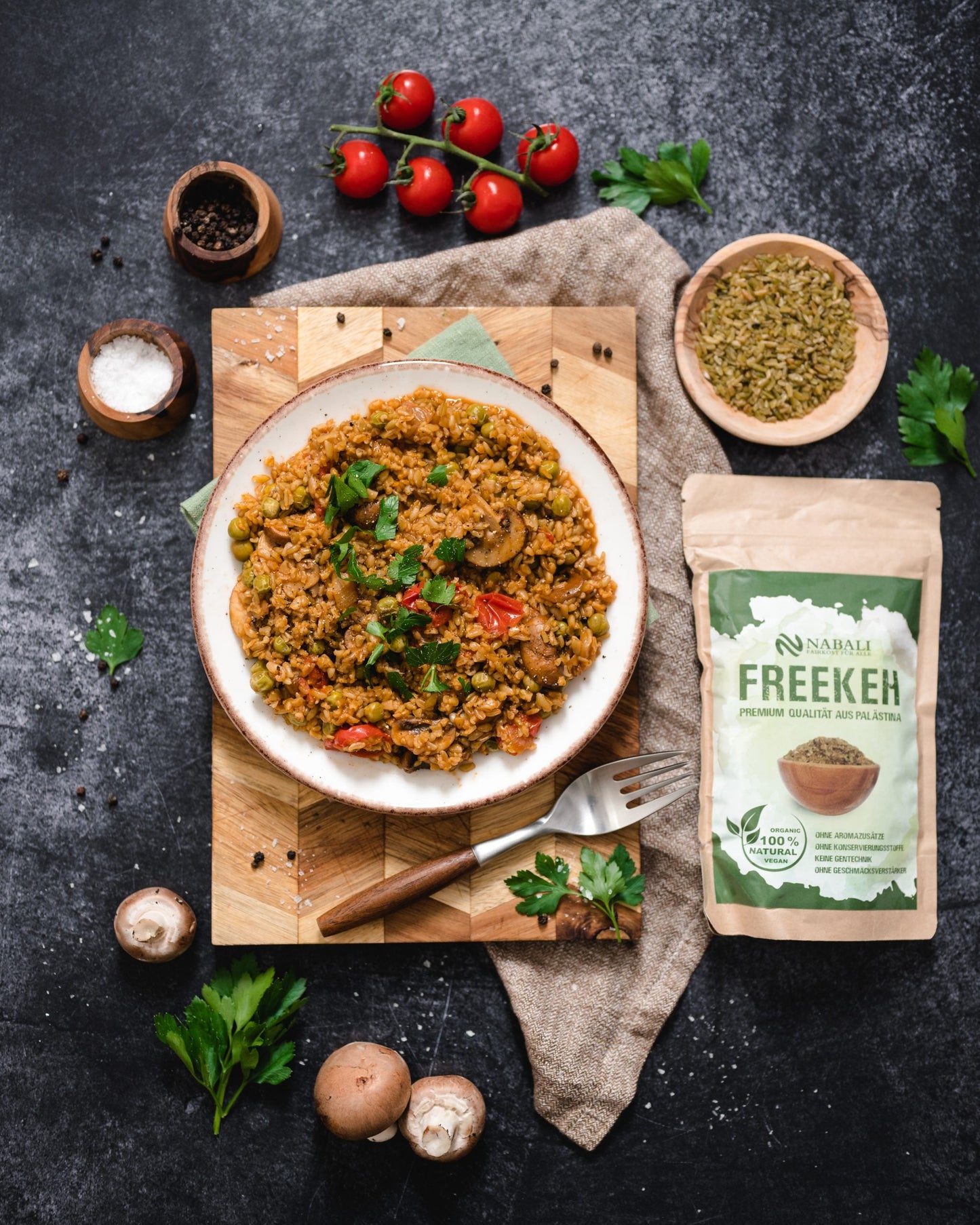 "Ein Teller Freekeh mit Gemüse und Kräutern, umgeben von frischen Zutaten und einer Packung Freekeh."