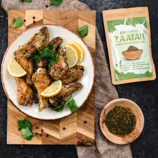 zatar Rezept: Hähnchenflügel mit Zaatar-Gewürz und Zitronenscheiben, serviert auf einem Teller, mit Zaatar-Gewürz auf einem Holzbrett im Hintergrund.