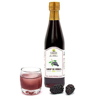 "Eine Flasche Brombeersirup, 25cl, mit goldenem Verschluss, neben einem Glas Sirup und frischen Brombeeren.\t"