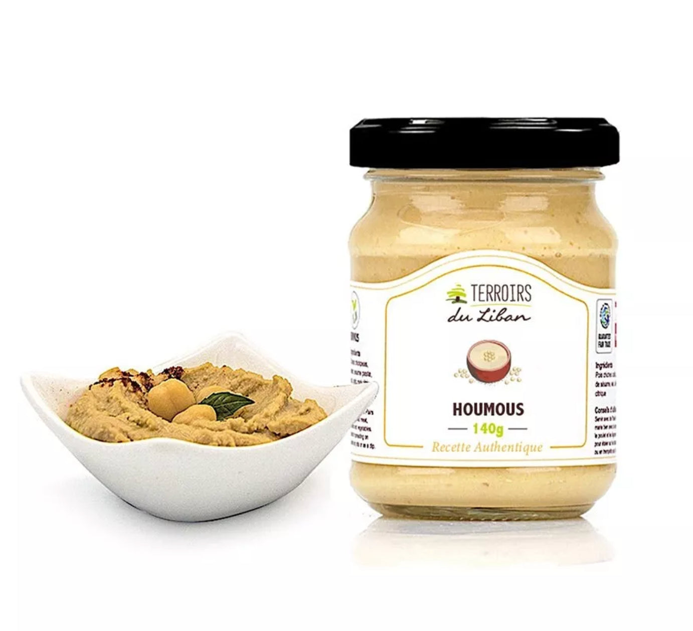 "Ein Glas Hummus neben einer Schale mit serviertem Hummus, dekoriert mit Kichererbsen und Kräutern.\t"